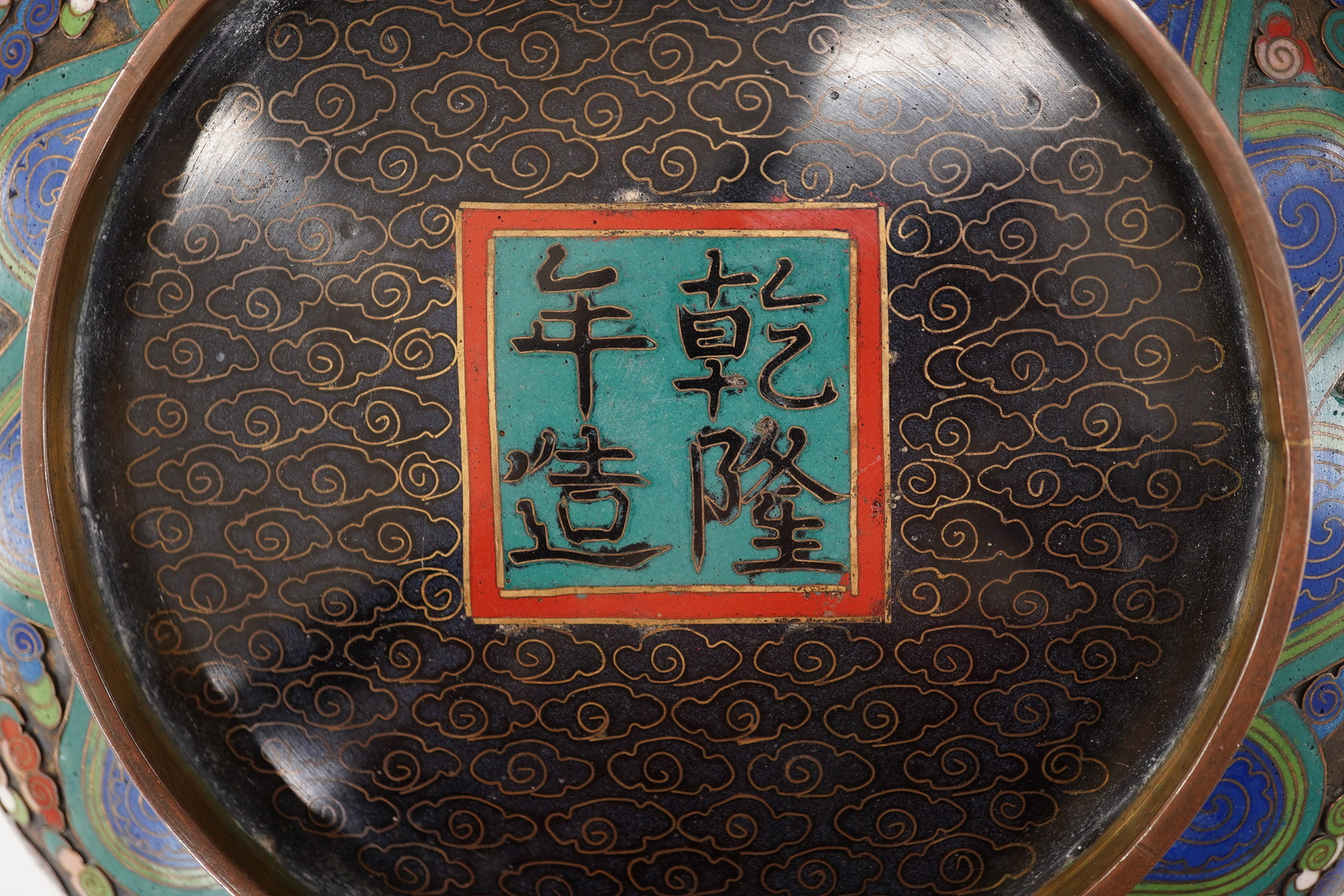 A Chinese cloisonné enamel ‘dragon’ bowl, Qianlong mark but early 20th century, on hardwood stand, 20cm diameter. Condition - poor to fair